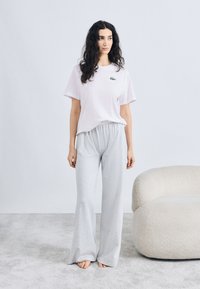 Camiseta de algodón rosa con logotipo verde, combinada con pantalones de chándal sueltos de color gris claro. Textura suave y ajuste relajado. Diseño minimalista.