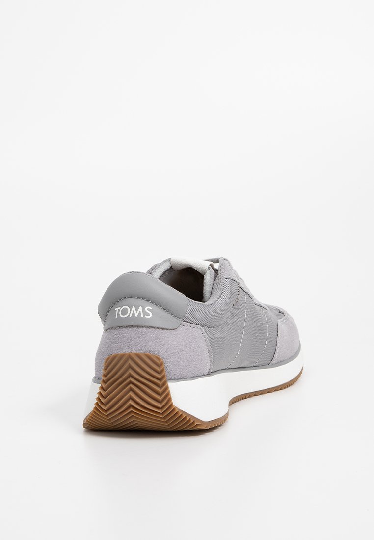 Chaussure de sport grise avec un tissu texturé, des accents lisses, une semelle blanche et une semelle extérieure en caoutchouc antidérapante ; présente un logo à l'arrière.