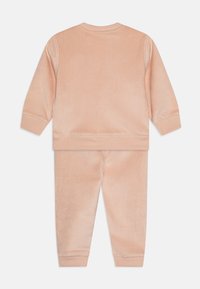 Peachfarget kordfløyels to-delt sett med langermet topp og matchende bukser med ribbet tekstur og elastiske mansjetter.