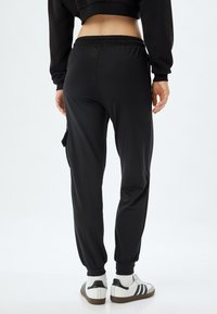 Zwarte joggingbroeken met een elastische tailleband, taps toelopende boorden en zijzakken. Gecombineerd met witte sneakers met zwarte accenten.
