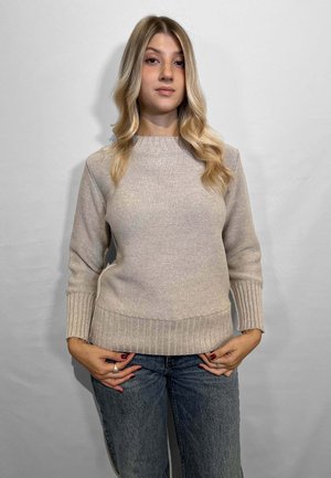 Maglione beige chiaro con lavorazione a maglia testurizzata, polsini e orlo a coste. Abbinato a jeans blu casual, presenta un collo rotondo.