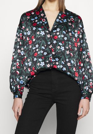 Sort blomsterbluse med røde og blå blomster på et grønt vinstokmønster, med en løs pasform og lange ærmer. Glat stoftekstur.
