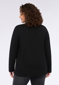 Bluză neagră cu mâneci lungi, confecționată dintr-un material neted, cu o croială lejeră, având un decolteu rotund și fante laterale la tiv pentru un plus de libertate de mișcare.