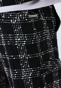 Pantaloni in tessuto textured bianco e nero con un motivo a quadri e un piccolo etichetta metallica "Project X Paris" vicino alla tasca.