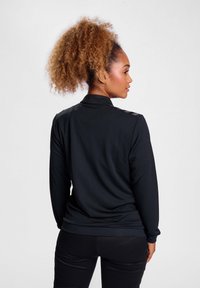 Schwarzes Langarmoberteil mit Kragen, aus einem strukturierten Stoff gefertigt. Verfügt über dezente Schulterakzente und ein tailliertes Design.
