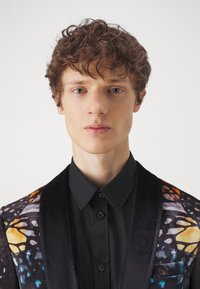 Black shirt under a patterned jacket featuring butterfly designs in orange, blue, and black, with a smooth texture and a satin finish.