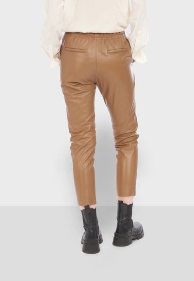 Pantalons en simili cuir marron avec un design ajusté, une taille élastique et deux poches arrière. Associés à des bottines noires.