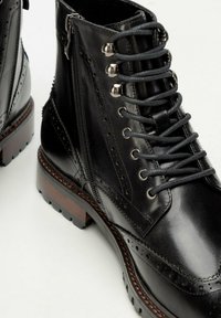 Botas de tobillo de cuero negro con perforaciones decorativas, ojales de metal y cordones, con cremalleras laterales y un resistente tacón de madera.