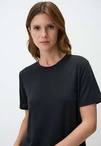 T-shirt nera a girocollo in un tessuto leggero e morbido, con maniche corte, aderente alle spalle e una silhouette rilassata.