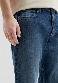 Jeans in denim blu scuro con una texture liscia, vestibilità regolare, design a cinque tasche e dettagli di cucitura a contrasto.