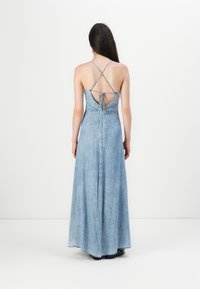 Svijetloplavi denim maxi haljina s dubokim izrezom na leđima, ukriženim trakama i detaljem za vezanje. Lepršava suknja s opuštenim krojem i suptilnom teksturom.