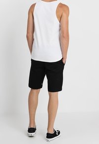Canottiera bianca senza maniche, pantaloni corti neri e sneakers nere. Design semplice, colori solidi, tessuto di cotone e nessun modello o grafica visibile.