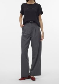 Blouse noire à manches courtes avec détail découpé, associée à un pantalon large taille haute gris et des chaussures plates rouges. Tissu lisse et coupe ajustée.