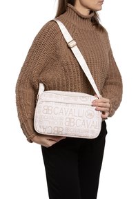 Borsa a spalla beige con motivo a logo in rilievo, tessuto liscio e forma rettangolare. Ha una tracolla spessa e regolabile con dettagli in metallo.