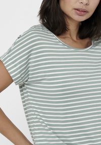 T-shirt rayé en vert pâle et blanc, fabriqué en coton doux. Présente un col rond et des manches courtes, avec des détails de couture visibles.