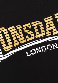 Black cotton t-shirt featuring bold gold and white graphics with the text "LONSDALE" and "LONDON." Text has a striped design and varying thickness.