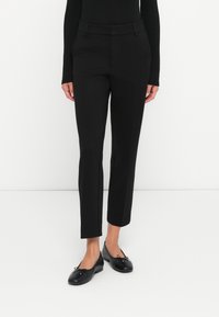 Čierne nohavice na mieru so slim fit strihom, vyrobené z hladkej tkaniny, s pútkami na opasok a skrátenou dĺžkou nad členkom. Spárované s čiernymi balerínami.