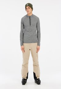 Grijze lange mouw ritshemd met een opstaande kraag, gecombineerd met beige skibroeken en zwarte skischoenen. De kenmerken zijn minimaal en functioneel.