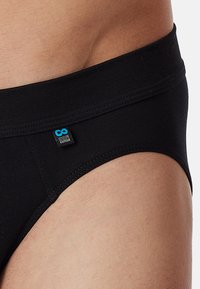 Schwarze Baumwollslips mit einem glatten Bund und einem blauen Etikett mit der Aufschrift "Lifelong Cotton". Dezente Nähedetails an den Beinausschnitten.