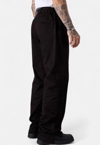 Black cargo pants made of durable fabric. Features an elastic waistband, side pockets, and a back pocket with a square design detail.