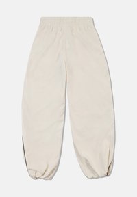 Beige pants with elastic waist and tapered design, gathered at the ankles, offering a smooth texture. Includes side slits for ease of movement.