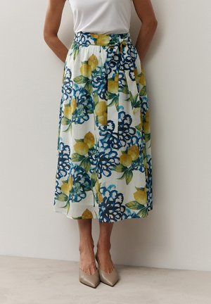 Weißer Midirock mit gelbem Zitronen- und blauem Blumenmuster, gebundener Taillengürtel, getragen mit beigen spitzen Schuhen und weißem ärmellosem Oberteil.