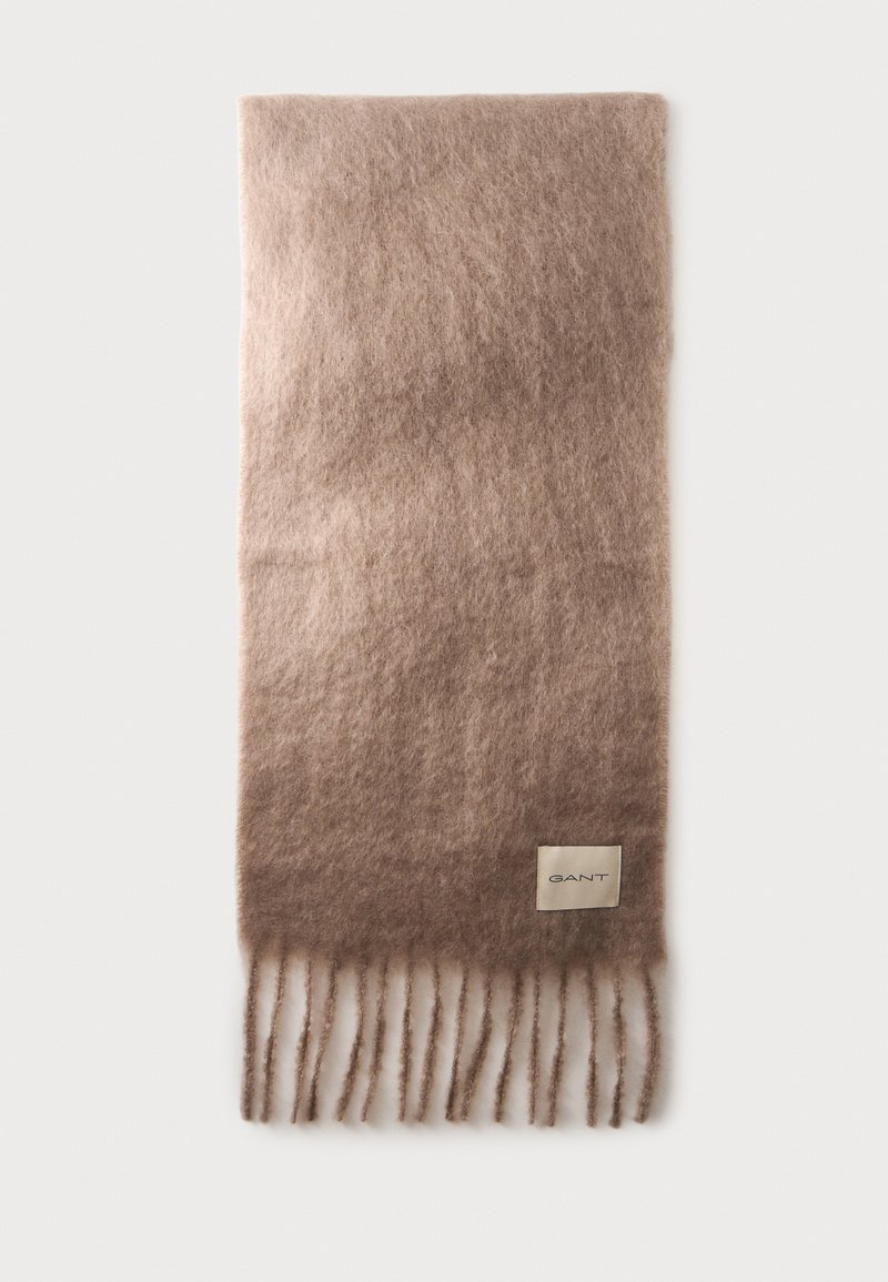 Écharpe en laine marron clair douce avec des extrémités à franges et une petite étiquette beige indiquant "GANT" près d'un bord.