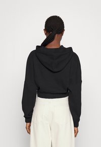 Czarna krótka bluza z kapturem z centralnym szwem na plecach, dużym kapturem i szerokimi rękawami, zestawiona z jasnymi, wysokim stanem spodniami.