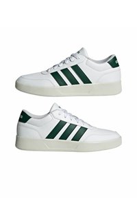 Zapatillas blancas con rayas verdes, parte superior de cuero suave, puntera redonda y suela acolchada. Incluyen cordones y un logotipo en el talón.