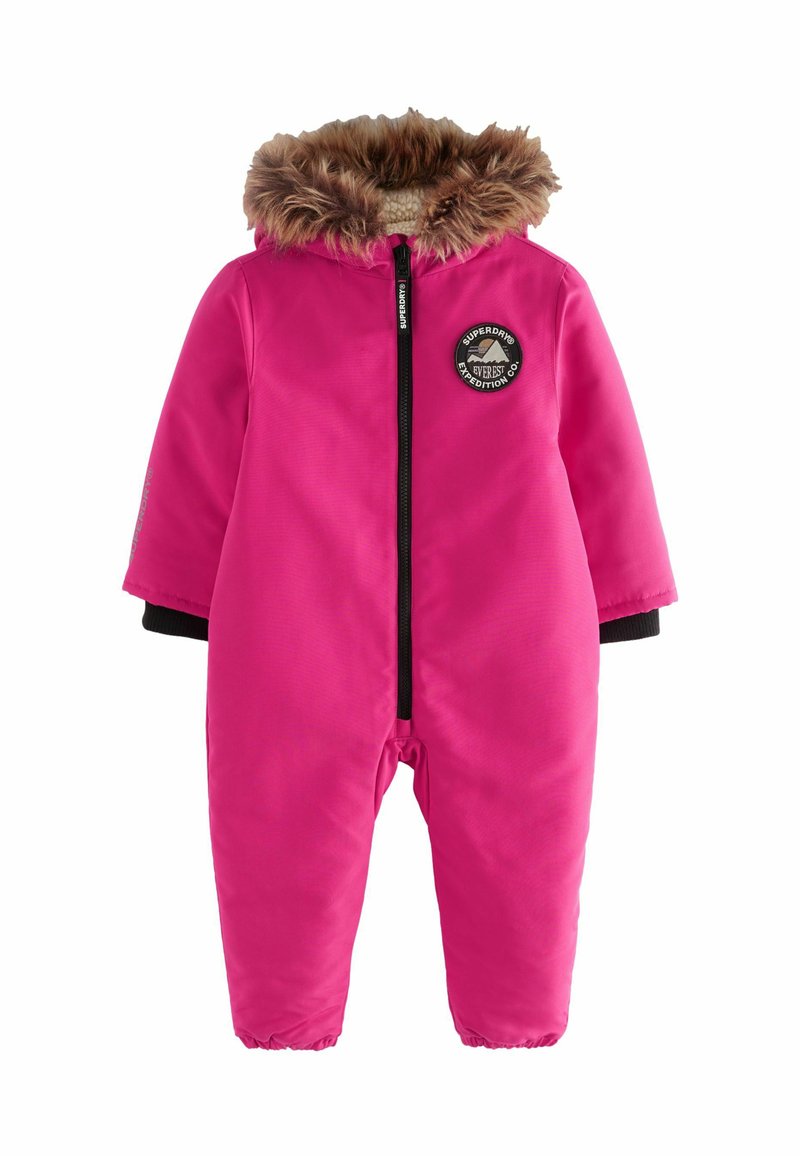 Combinaison de neige isolée rose avec des bords côtelés noirs, une capuche en fausse fourrure, une fermeture éclair à l'avant et des détails de patch logo. Tissu extérieur lisse.