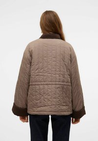 Polstret jakke i lys brun med quiltet design og brune detaljer. Har høj krave og brede ærmer, hvilket giver en afslappet pasform.
