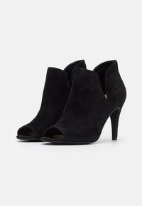Botines de ante negro abiertos en la parte delantera, con una silueta curva, tacón alto de aguja y cortes laterales para un diseño moderno.