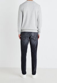 Pull gris à encolure ronde, poignets et ourlet côtelés, associé à un jean gris foncé avec des surpiqûres discrètes sur les poches arrière et des baskets blanches.