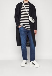 Abrigo negro, suéter a rayas, jeans azules y zapatillas blancas de lona con rayas negras. Bolsa bandolera con diseño geométrico.