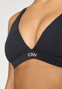 Μαύρο τριγωνικό bralette με μαλακό ύφασμα, σχέδιο σε σχήμα V και ελαστική ζώνη με το λογότυπο "ICIW". Λείο υφή χωρίς ορατές διακοσμήσεις.