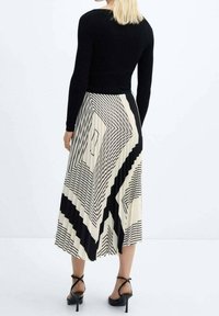 Top lungo a maniche lunghe ribbed nero abbinato a una lunga gonna plissettata con un motivo geometrico in bianco e nero, indossato con sandali con tacco alti neri.