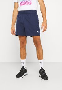 Navy athletic shorts with an elastic waistband, featuring a white Puma logo. Worn with black sneakers and white socks with Puma accents.