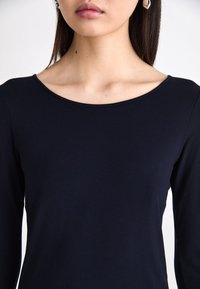 Marineblauw langemouwen top met een brede, ronde halslijn. Zachte, gladde stof, slim fit ontwerp, geaccentueerde schouders, geen zichtbare patronen.