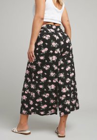 Pantaloni larghi floreali neri con motivi di rose rosa. Vita elastica, tessuto leggero, lunghezza cropped e spacchi laterali per facilità di movimento.