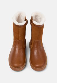 Bottines en cuir brun avec doublure en fausse fourrure, surface lisse, et fermetures éclair latérales pour un enfilage facile. Des accents en suede rehaussent la texture et le design.