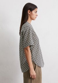 Blouse à manches courtes, à motifs noir et blanc, avec une coupe ample et des fentes sur les côtés. Tissu lisse avec un design géométrique abstrait.