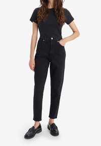 Svarta högmidjade jeans med rak bendesign, med knappgylf och fem fickor, ihop med en åtsittande svart t-shirt och loafers.