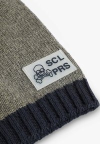 Gorro de lana con un diseño en gris y azul marino, con una banda acanalada y un parche rectangular que muestra una calavera y huesos cruzados con el texto "SCL PRS".
