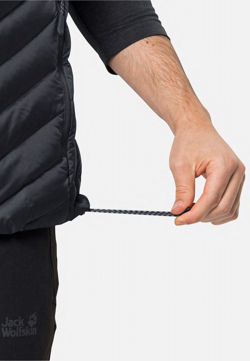 Schwarze isolierte Weste mit Zickzack-Steppung; Hand, die an einem Zugband am unteren Ende greift; mit einem Reißverschluss und elastischen Beschlägen zur Anpassung.