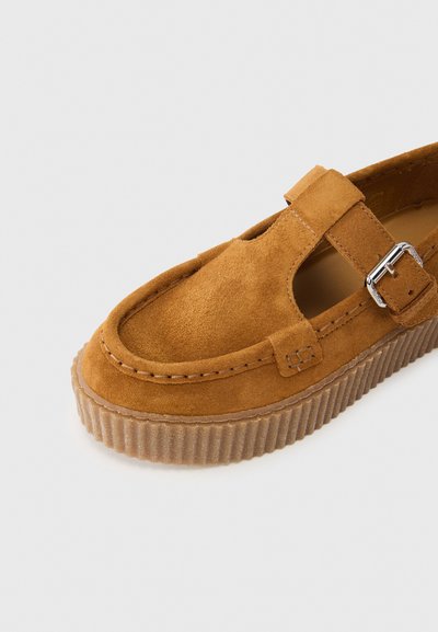 Chaussure en daim marron avec une semelle plateforme superposée, dotée d'une bride à l'avant avec boucle métallique, bout arrondi et surface texturée.