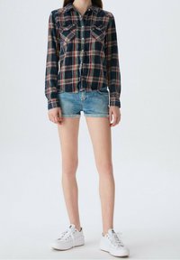 Granatowa i czerwona koszula w kratę z dwiema kieszeniami na piersi, zestawiona z jasnoniebieskimi szortami dżinsowymi. Model nosi białe sneakersy. Swobodny strój.