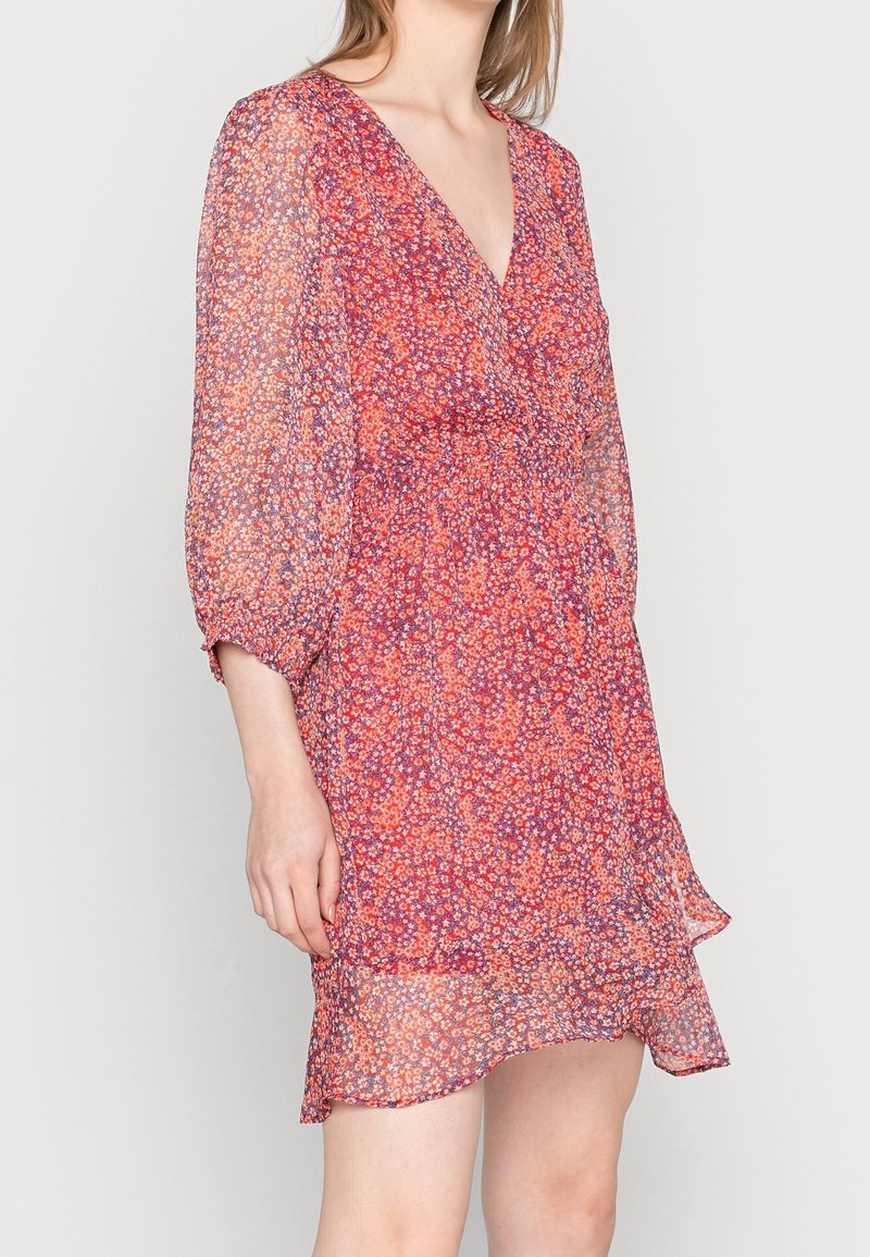 Robe à imprimé floral dans des tons rouges et violets, fabriquée en tissu léger ; présente un col en V, une taille élastique et un ourlet à volants.