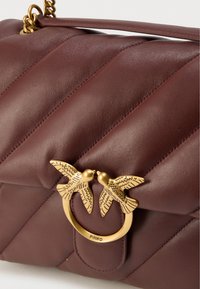 Τσάντα χειρός από δέρμα μπορντό με κεντητό σχέδιο, διαθέτει κούμπωμα σε σχήμα χρυσού πουλιού και λουρί με αλυσίδα. Ομαλή υφή και εμφανείς λεπτομέρειες ραφής.