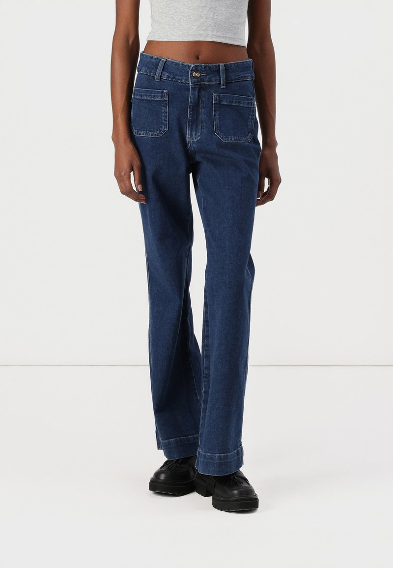 Modre jeans hlače z ravnim nogavicami, visokim pasom, dvema sprednjima žepoma in dvema zadnjima žepoma. Zaključene z gumbom in zadrgo.