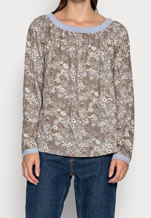 Person iført en langærmet blomsterbluse med lyseblå krave og manchetter, kombineret med mørkeblå denimjeans.